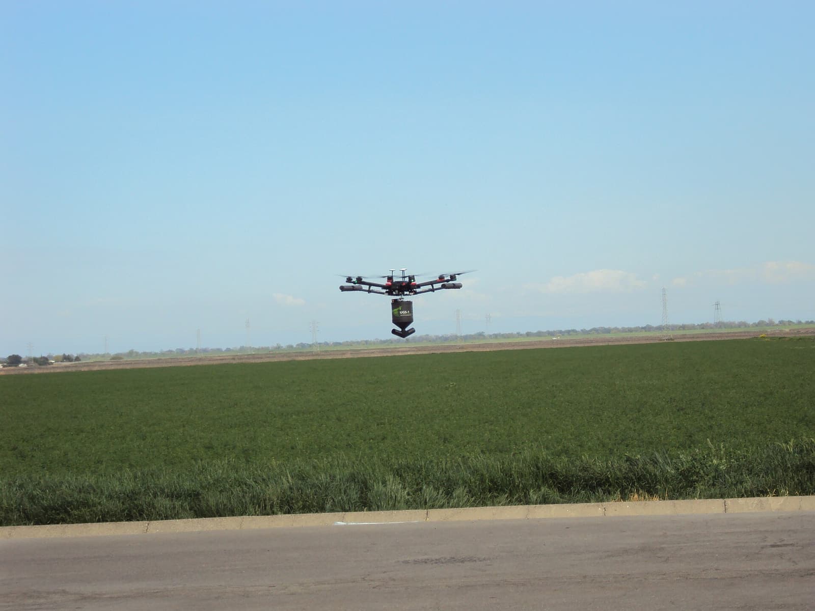 An agricultural spray drone hovering over a green crop field
