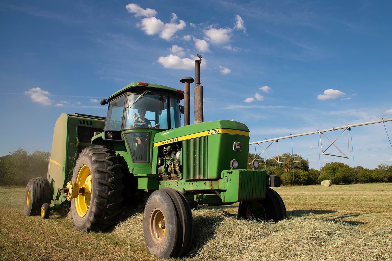 A green row-crop tractor pulling a baler in Texas
