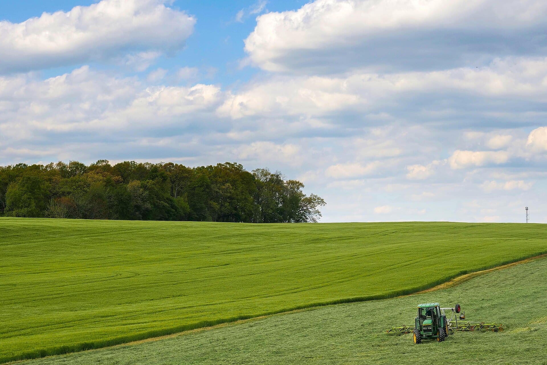 A tractor mowing a green hayfield under a wide sky in Maryland